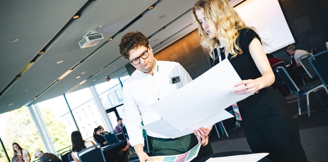 Wes Hiatt and Isabelle O'Toole standing next to one another reviewing poster responses in a conference room.